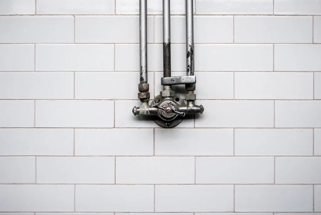 Exposed water pipes and valve on a white tile wall